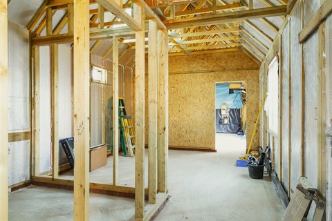Interior of house under construction with interior walls unfinished and roof beams showing.
