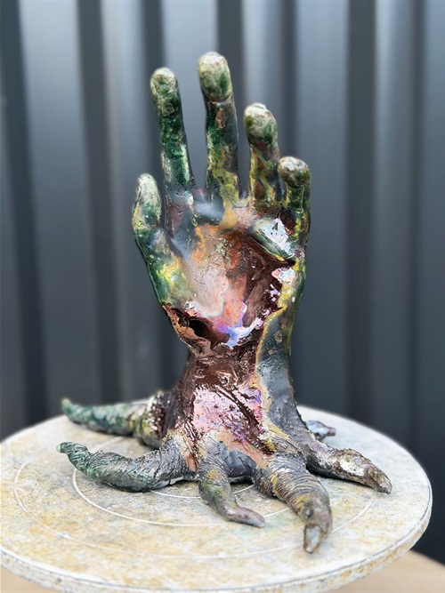 A sculpture of a hand reaching upwards towards the sky. The bottom of the hand has roots like a tree.