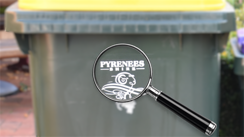 A recycle bin with yellow lid, with a magnifying glass focused on the Pyrenees Shire Council logo