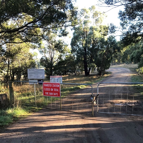 A country road with a set of gates at the front. Signs on the gate indicating for a transfer station. 
